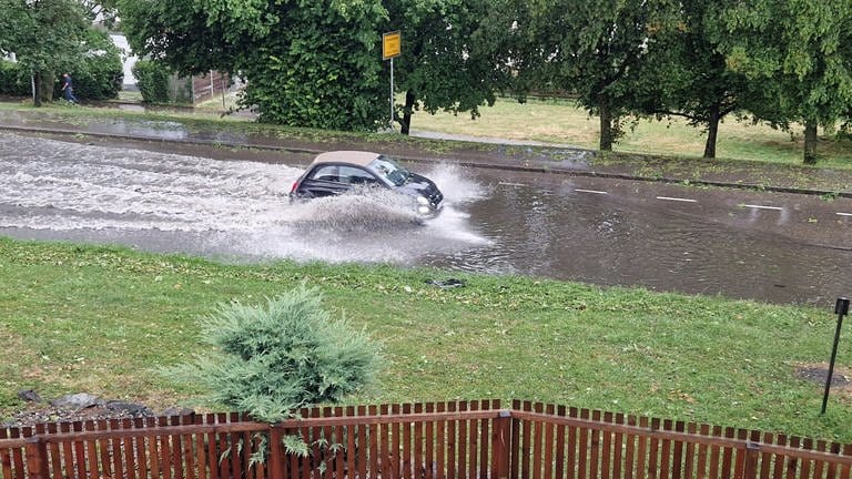 Ein Auto pflügt nach einem Gewitter durch eine überflutete Straße. Ein kleines Auto verschwindet fast in den Wassermassen nach dem Starkregen an der Böfinger Halde in Ulm.