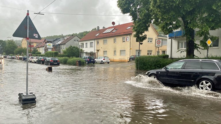 Ein Auto fährt langsam über eine überflutete Straße. Nach dem Unwetter mit Hagel und Starkregen "schleicht" ein Auto durch die Wassermassen im Lehrer Tal in Ulm. 
