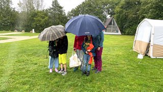 Fünf junge Camper auf einem Zeltplatz in Laichingen verstecken sich unter Schirmen, um dem Regen zu entkommen.