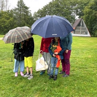 Fünf junge Camper auf einem Zeltplatz in Laichingen verstecken sich unter Schirmen, um dem Regen zu entkommen.