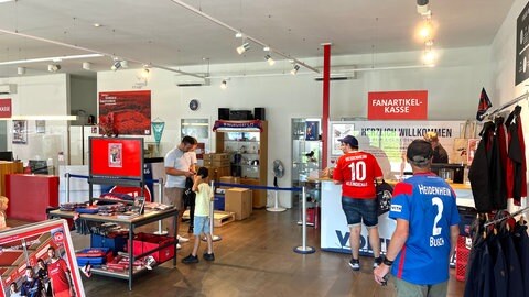 Menschen in Fußballtrikots sehen sich in einem Laden für Fanartikel um. Im Fanshop des FC Heidenheim werden fleißig Fan-Artikel  gekauft: Die Fans fiebern dem ersten Bundesliga-Spiel in der Vereinsgeschichte des 1. FC Heidenheim entgegen. 