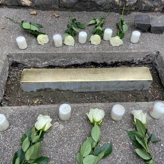 Kerzen und Blumen vor der neuen Stolperschwelle in Aalen-Wasseralfingen - Zum Gedenken an KZ-Häftlinge hat der Künstler Demnig am Samstag (26.8) eine sogenannte Stolperschwelle verlegt. Anders als Stolpersteine wird sie an eine Gruppe von Opfern erinnern.