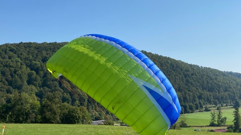 Ein hellgrüner Gleitschirm bei der Landung auf dem Rasen in Schelklingen-Hütten (Alb-Donau-Kreis) - hier gibt es einen idealen Übungshang für Lernende der Flugschule Ulm.