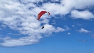 Ein rot-weißer Gleitschirm schwingt lautlos durch die Wolken. Mit 78 Jahren ist der Gleitschirmlehrer in Schelklingen (Alb-Donau-Kreis) immer noch mit Leidenschaft am Start.  (Symbolbild).