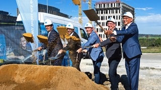 Männer im Anzug und mit Bauhelmen auf den Köpfen werfen mit Spaten Sand in die Luft. Zum gemeinsamen Spatenstich für das neue Rechenzentrum der SWU Stadtwerke UlmNeu-Ulm versammelten sich im Ulmer Science Park III: Klaus Eder (Geschäftsführer SWU Stadtwerke UlmNeu-Ulm), Adrian Hochstrasser (Geschäftsführer hochstrasser gesellschaft für architektur mbh), Christian Tigges (Projektleiter DC-Datacenter-Group GmbH), Michael Beuschlein (Geschäftsführer SWU TeleNet GmbH) und Gunter Czisch (Oberbürgermeister Ulm).