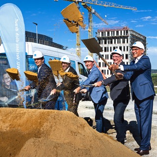 Männer im Anzug und mit Bauhelmen auf den Köpfen werfen mit Spaten Sand in die Luft. Zum gemeinsamen Spatenstich für das neue Rechenzentrum der SWU Stadtwerke UlmNeu-Ulm versammelten sich im Ulmer Science Park III: Klaus Eder (Geschäftsführer SWU Stadtwerke UlmNeu-Ulm), Adrian Hochstrasser (Geschäftsführer hochstrasser gesellschaft für architektur mbh), Christian Tigges (Projektleiter DC-Datacenter-Group GmbH), Michael Beuschlein (Geschäftsführer SWU TeleNet GmbH) und Gunter Czisch (Oberbürgermeister Ulm).