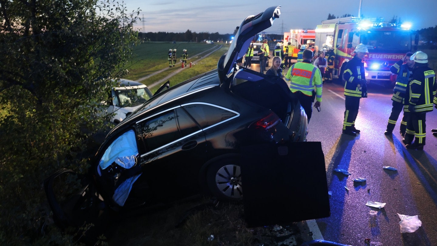 Zwei Unfallwagen in einem Graben und einem Feld, auf der Straße viele Rettungsfahrzeuge, ein Feuerwehrauto mit Blaulicht und viele Rettungskräfte. Bei Neu-Ulm-Holzschwang ist eine 19-jährige Autofahrerin in den Gegenverkehr geraten und hat einen schweren Unfall verursacht. Vier Menschen wurden verletzt.