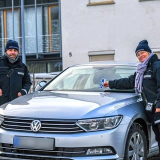 Zwei Mitarbeiter des Ordnungsamtes stehen auf einem Parkplatz in Giengen an der Brenz im Landkreis Heidenheim. Wer derzeit richtig parkt, bekommt Schokolade als Knöllchen.