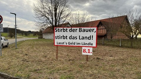 Auf einer Wiese bei Sachsenhausen (Kreis Heidenheim) kündigt ein Protestschild den Aktionstag der Landwirte am 8. Januar an. Darauf ist zu lesen: "Stirbt der Bauer, stirbt das Land! Lasst's Geld im Ländle." 