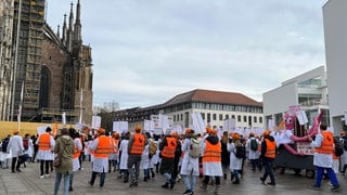 Ärztinnen und Ärzte der Uniklinik Ulm, teils in weißen Kitten, stehen mit Transparenten vor dem Ulmer Münster. Sie haben am Dienstagmittag für bessere Arbeitsbedingungen an der Uniklinik demonstriert. 