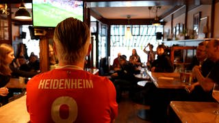 Während des Spiels müssen seine Frau und sein Sohn bedienen. Wirt Frank Zeger sitzt im Trikot gebannt vor dem Bildschirm. Auch die anderen Gäste im Café Melange fiebern mit, während der FC Heidenheim bei Union Berlin spielt.