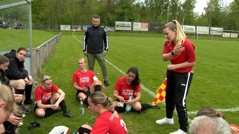 In der Halbzeitpause motiviert Trainerin Ann-Kathrin Schwer ihre Mannschaftskolleginnen, die vor ihr erschöpft auf dem Boden sitzen. 