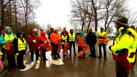 Gruppe Menschen steht in Regenmänteln gekleidet auf einem Waldparkplatz in Heidenheim.