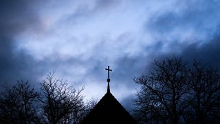 Dunkle Wolken ziehen über das Kreuz auf einer evangelischen Kirche in der Region Hannover hinweg. 