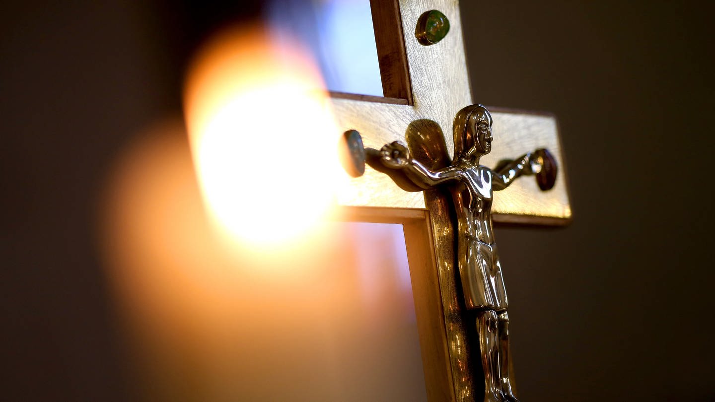 Kruzifix vor einer Kerze. Die Diözese Rottenburg/Stuttgart muss sich mit Missbrauchsvorwürfen auseinandersetzen.