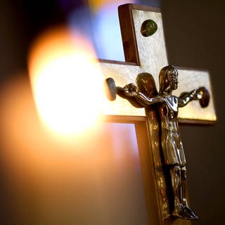 Kruzifix vor einer Kerze. Die Diözese RottenburgStuttgart muss sich mit Missbrauchsvorwürfen auseinandersetzen.