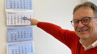 Prof. der Aktuarwissenschaften an der Uni Ulm zeigt lachend im Kalender auf Freitag, 13.  