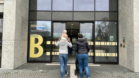 Zwei Frauen, das Kind sitzt auf den Schultern der einen, die andere schiebt den Kinderwagen. Die Pflegeeltern sind mit ihrem 9-Monate altem Pflegekind auf dem Weg ins Jugendamt des Alb-Donau-Kreises.