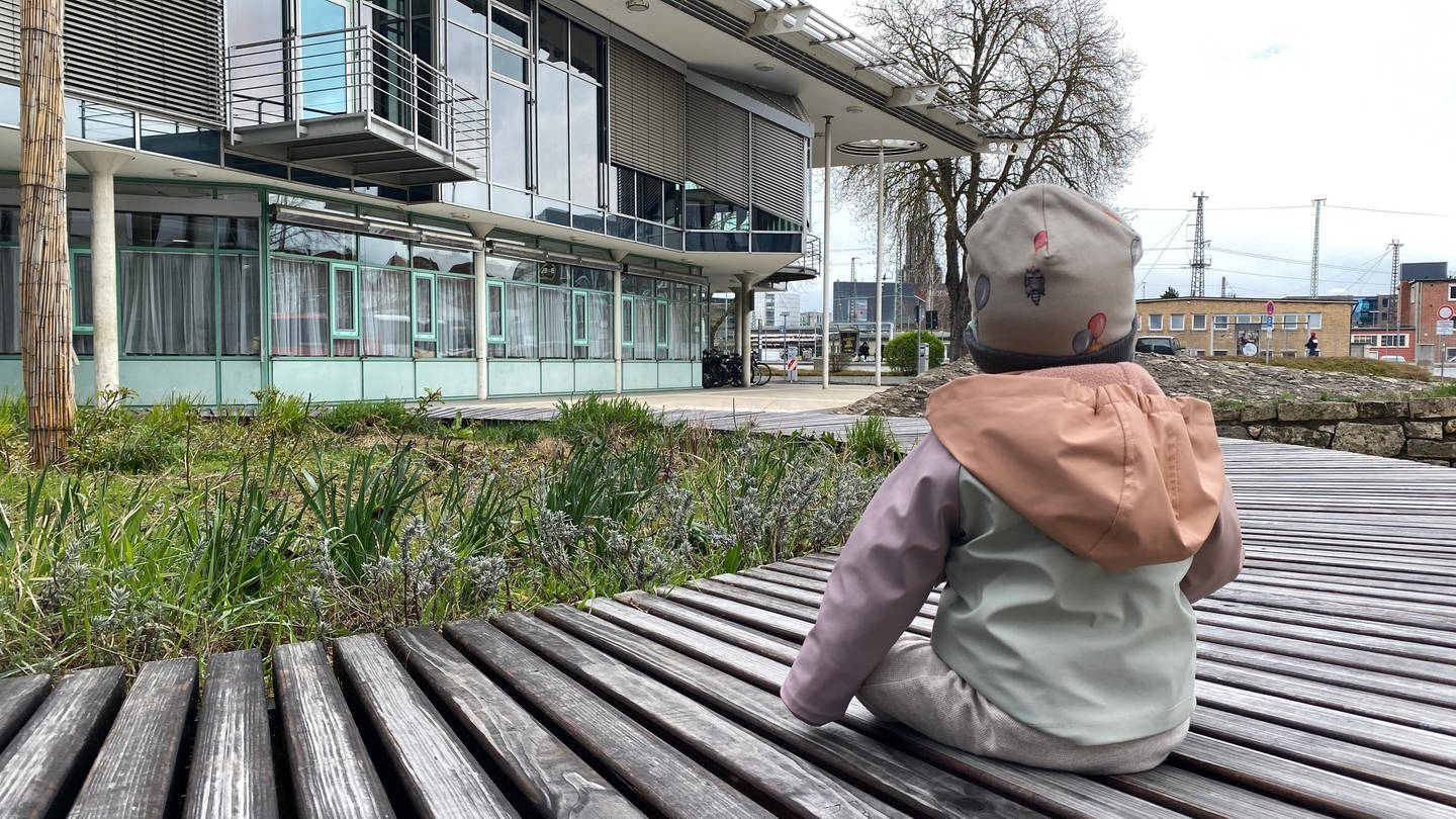 Das 9-Monate alte Pflegekind sitzt auf einer Bank vor dem Landratsamt des Alb-Donau-Kreises.