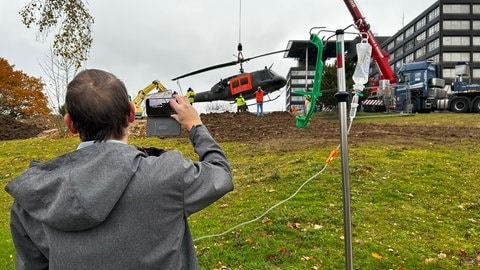 Ein Patient mit Infusionsständer steht vor dem Hubschrauber und macht ein Foto