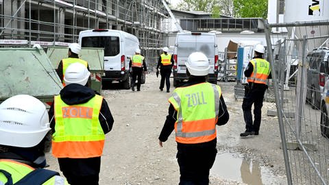 Menschen in leuchtenden Westen mit der Aufschrift Zoll nähern sich einer Baustelle. 25 Ermittlerinnen und Ermittler des Hauptzollamtes Ulm haben am Dienstag Baustellen im Ulmer Dichterviertel auf Schwarzarbeit hin kontrolliert. 