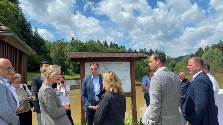 Frauen und Männer vor einer Informationstafel vor einem Rückhaltebecken. Die baden-württembergische Umweltministerin Thekla Walker (links) und Bundesumweltministerin Steffi Lemke (beide Grüne) waren in Täferrot, um sich über den Hochwasserschutz im Ostalbkreis zu informieren. 