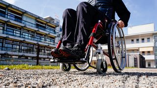 Ein Mann vor einem Klinikgebäude in einem Rollstuhl auf einem Kiesweg. Nach seiner Behandlung im Krankenhaus in Ehingen im Alb-Donau-Kreis hat ein Patient einen Rollstuhl geklaut. (Symbolbild)