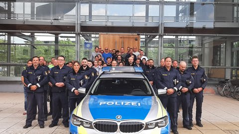 Polizistinnen und Polizisten stehen an  einem Einsatzfahrzeug. Etwa 60 Polizistinnen und Polizisten in Neu-Ulm haben sich am Freitag der landesweiten Schweigeminute für ihren in Mannheim getöteten Kollegen angeschlossen. 