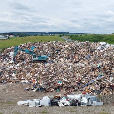 Ein riesiger Sperrmüllberg mit einem Bagger, der fast darin verschwindet: Im Kreis Günzburg sind inzwischen 25.000 Kubikmeter Hochwasser-Müll gesammelt worden.