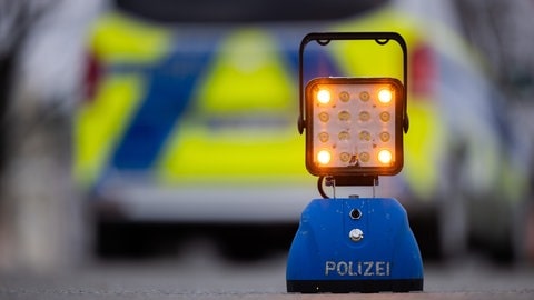 Ein Warnlicht mit der Aufschrift "Polizei" steht auf der Straße vor einem Einsatzfahrzeug der Polizei (Symbolbild).