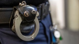 Handschellen am Gürtel eines Polizisten - drei 18-Jährige wurden wegen versuchter Tötung in Schwäbisch Gmünd festgenommen. 