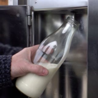 Im Hintergrund hält eine Hand eine Flasche, die von einem Automaten mit Rohmilch befüllt wird. Im Vordergrund die Anzeige, wieviel Rohmilch bereits abgegeben wurde. Influencer in den sozialen Medien werben aktuell für den Verzehr von Rohmilch. 