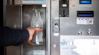 Eine Flasche wird an einem Automaten mit Rohmilch befüllt. Darüber ein Hinweisschild, die Milch solle vor dem Verzehr erhitzt werden. 