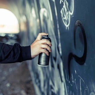 Eine Männerhand sprüht mit einer Spraydose etwas an eine Wand. (Symbolbild)