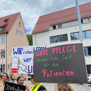 Pflegekräfte halten Plakate mit Forderungen für bessere Arbeitsbedingungen und mehr Lohn in die Höhe. Beschäftigte an der Uniklinik Ulm streiken für mehr Lohn und bessere Arbeitsbedingungen.