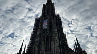 Das Banner am Münsterturm und Polizeiautos. Klimaaktivisten sind am Dienstagfrüh am Ulmer Münsterturm hochgeklettert und haben ein Banner entrollt. Die Polizei versucht, die illegale Aktion zu beenden.