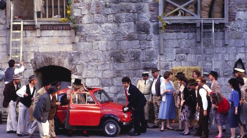 Männer schauen in ein rotes Auto - 1987 wird im Rittersaal von Schloss Hellenstein die Donizetti-Oper "Der Liebestrank" aufgeführt. In diesem Jahr sind die Opernfestspiele Heidenheim 60 Jahre alt.