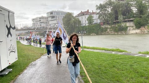 Im Regen laufen die Menschen mit den Fahnen vom Donaufest an der Donau in Ulm entlang. 