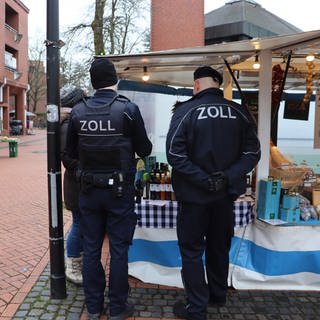 Zwei Zollbeamte des Hauptzollamtes Ulm stehen vor einem Stand auf einem Wochenmarkt im Raum Ehingen im Alb-Donau-Kreis. (Symbolbild)