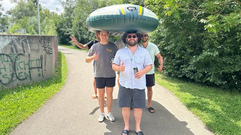 Fünf junge Männer machen sich mit einem Schlauchboot, das sie auf den Köpfen tragen, auf dem Weg zur Donau zum Nabada