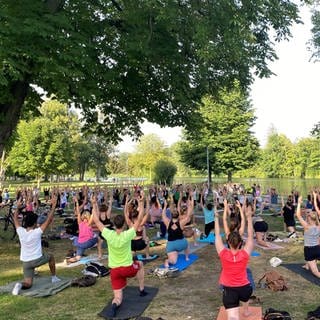 Ein Yogakurs in einem Park. Sport machen: Gemeinsam draußen und das auch noch kostenlos, das geht im Sommer in Ulm. Von Mai bis September bietet die Stadt Ulm kostenlose Sportkurse  wie Tanzen, Fitness, Selbstverteidigung in mehreren Parks an, und das sehr erfolgreich. Zu "Yoga auf Englisch" kommen oft mehr als 100 Teilnehmende.