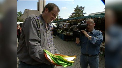 Johannes Mack im Jahr 2004: Er zeigt einem japanischen Kameramann seinen Stapel Unterschriften, die er für den Erhalt der Post in Blaustein gesammelt hat.
