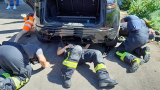 Drei Männer der Feuerwehr liegen unter einem Auto. Sie versuchen eine Babykatze zu retten, die in einem Auto auf einem Campingplatz in Laichingen eingeklemmt war. 