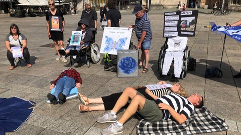 Mehrere Menschen liegen auf dem Münsterplatz in Ulm auf dem Boden. Mit der Liegend-Demo wollen sie auf das chronische Fatigue Syndrom oder auch MECFS aufmerksam machen und fordern eine bessere Behandlung. 