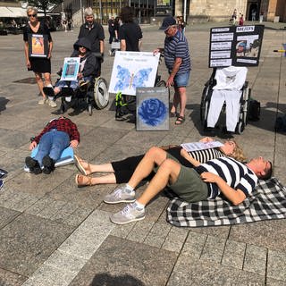 Mehrere Menschen liegen auf dem Münsterplatz in Ulm auf dem Boden. Mit der Liegend-Demo wollen sie auf das chronische Fatigue Syndrom oder auch MECFS aufmerksam machen und fordern eine bessere Behandlung. 