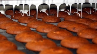 Runde Lebkuchen fahren auf einem Produktionsband unter eine Maschine, die weiße Glasur drauftropft (Archivbild). Allerdings produziert die Lebkuchenfirma Weiss in Neu-Ulm derzeit nicht: Alle drei Produktionsschichten sind am Mittwoch zum Warnstreik aufgerufen.