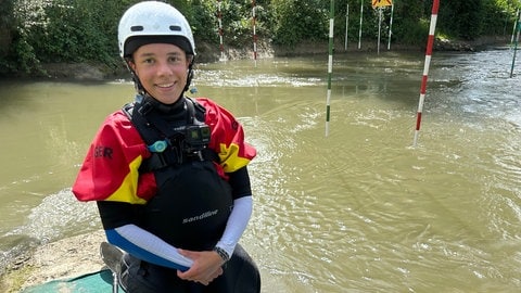 Pia Heinrich aus Erbach lächelt in die Kamera. Sie hat einen Helm auf und steht neben dem Illerkanal, in dem sie gleich Kanu-Freestyle übt. 