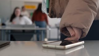 Eine Schülerin legt in einer Schule ihr Handy auf den Tisch. Ob Handys an Schulen genutzt werden dürfen, regelt jede Schule in Baden-Württemberg selber.