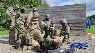 Soldaten in Tarnfarben und vermummt beugen sich über einen Soldaten am Boden: Ukrainische Soldaten auch ohne medizinische Ausbildung sollen lernen, Verletzte im Gefecht zu versorgen, so dass diese überleben.