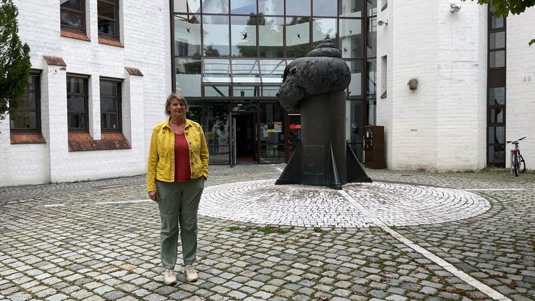 Naturschützerin Sabine Kröber steht auf einem gepflasterten Platz vor dem gläsernen Zwischenbau des Ulmer Landgerichts, der für Vögel kaum erkennbar sein dürfte.